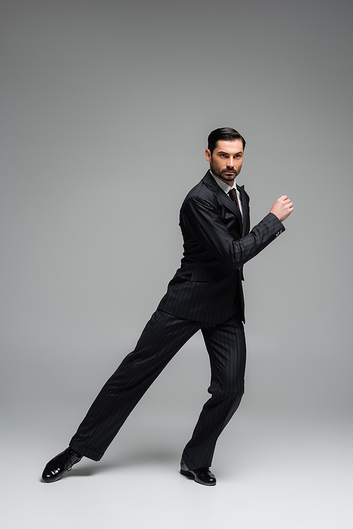 Professional dancer in suit performing tango on grey background