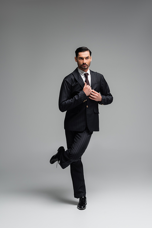 Elegant ballroom dancer adjusting jacket while performing tango on grey background