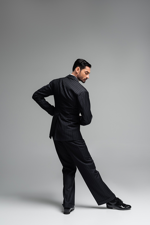 Side view of elegant dancer in suit moving on grey background