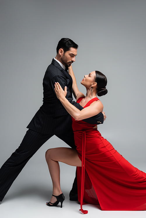 Brunette woman in dress dancing tango with partner on grey background