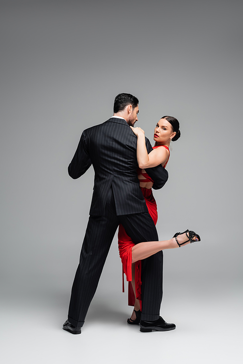 Full length of stylish dancer in heels performing tango with woman on grey background