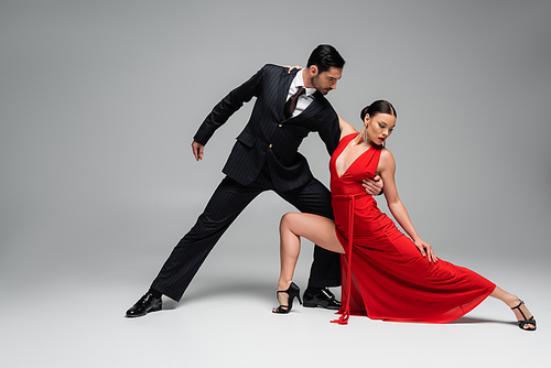 Man in suit hugging partner while dancing tango on grey background