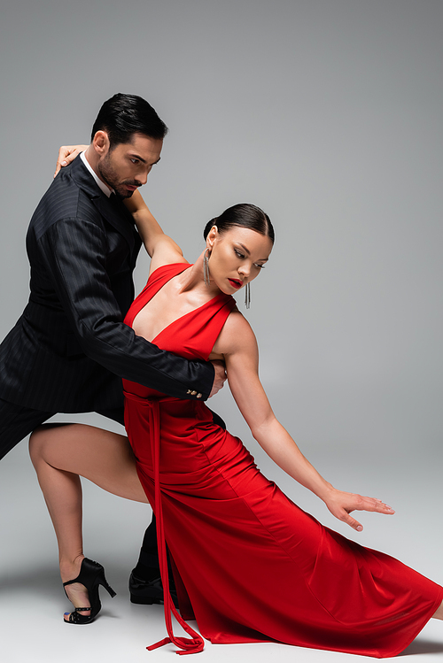 Man in elegant suit dancing tango with partner in dress on grey background