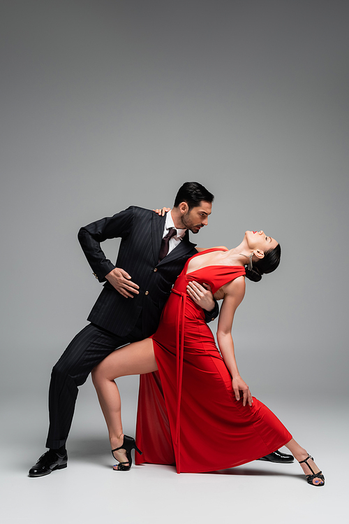 Side view of stylish partners dancing tango on grey background