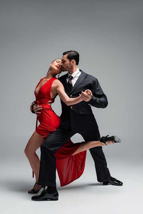 Full length of professional ballroom dancers performing tango on grey background