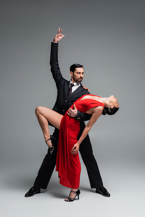 Elegant man posing while performing tango choreography with partner on grey background