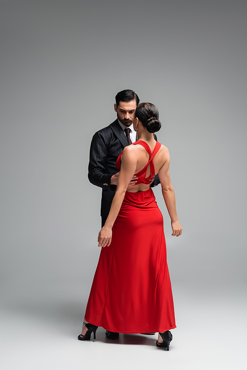 Dancer in suit hugging brunette partner in red dress on grey background