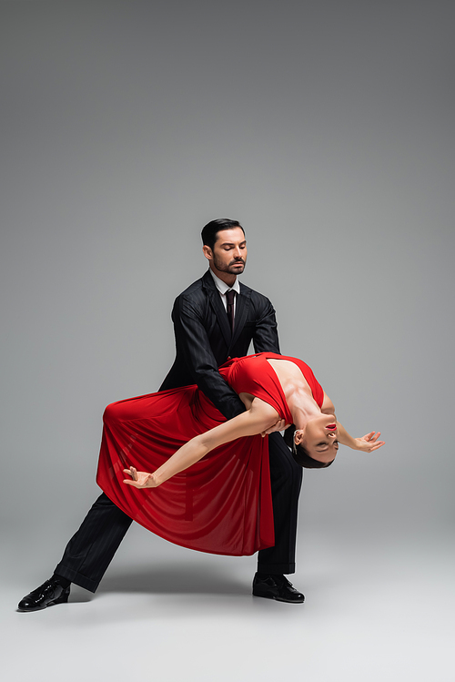 Full length of elegant couple dancing tango on grey background