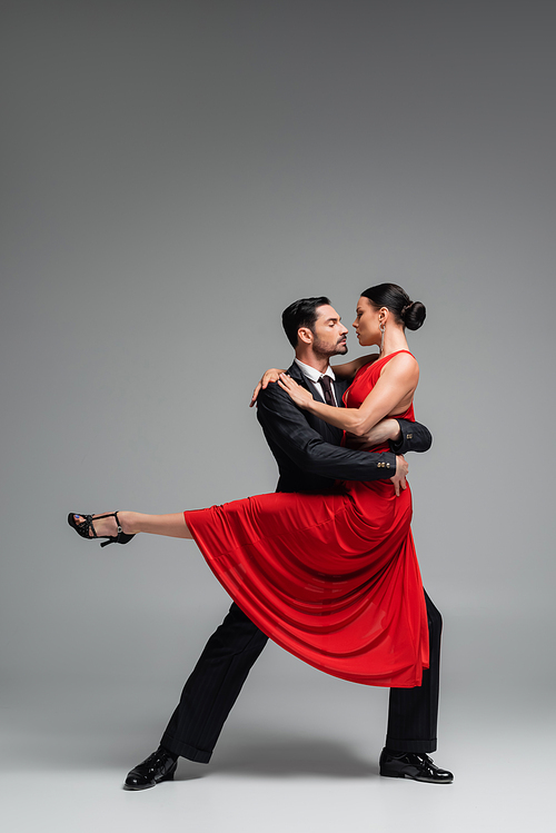 Side view of dancer holding partner in red dress on grey background