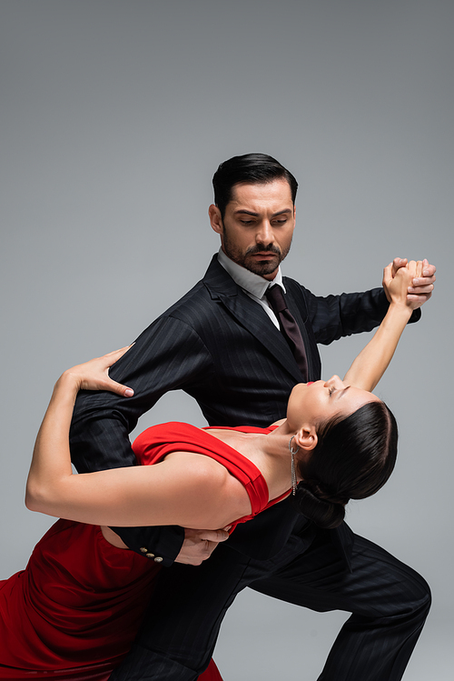 Man in suit dancing tango with brunette partner isolated on grey