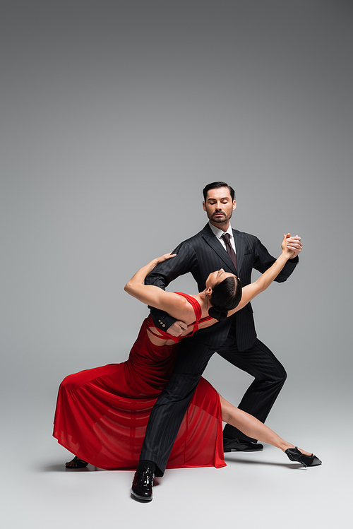 Dancer in suit performing tango with elegant partner on grey background