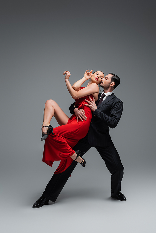 Full length of stylish couple performing tango on grey background