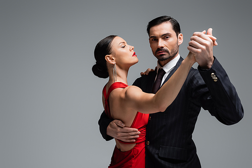 Man in suit looking at camera while dancing tango with partner isolated on grey