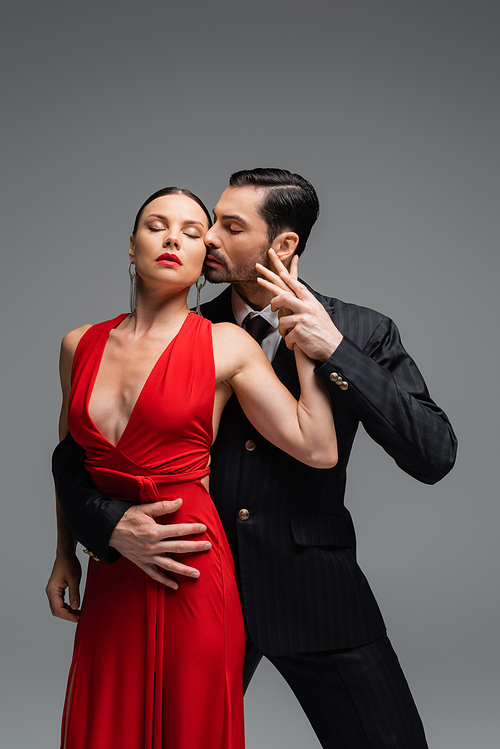 Passionate man in suit dancing tango with elegant partner isolated on grey