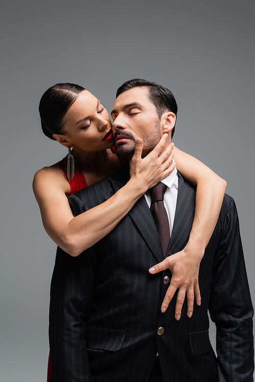 Brunette woman with red lips touching elegant man isolated on grey