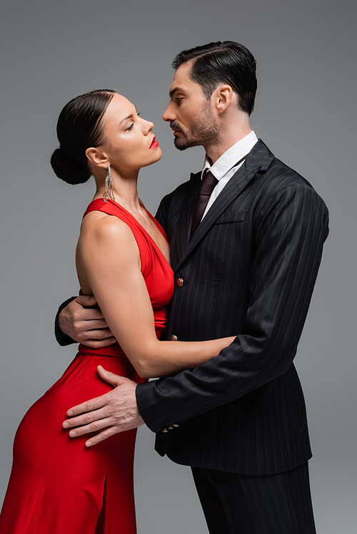 Side view of ballroom dancers hugging and looking at each other isolated on grey