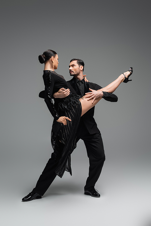 Professional dancers looking at each other while performing tango on grey background