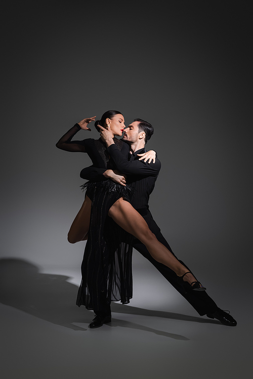 Side view of professional dancers performing tango on grey background with lighting