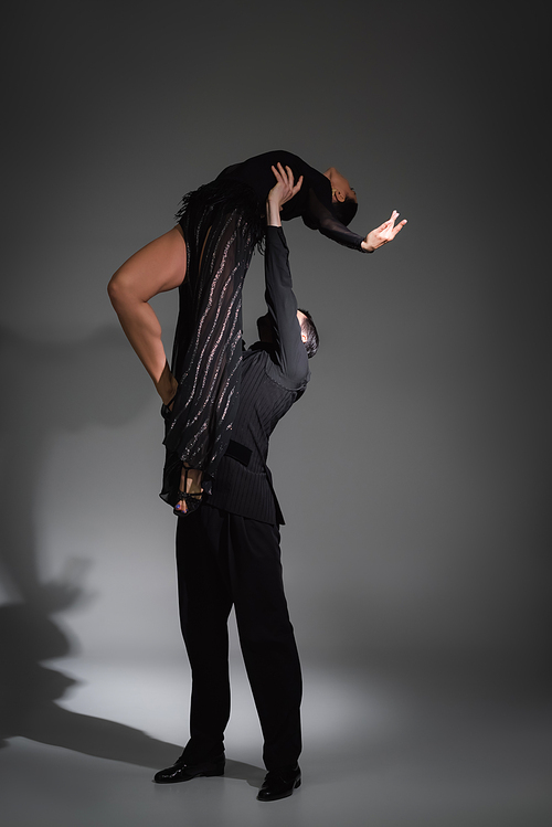 Dancer lifting partner in black dress on grey background with shadow