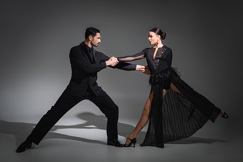 Side view of elegant couple performing tango on grey background with shadow