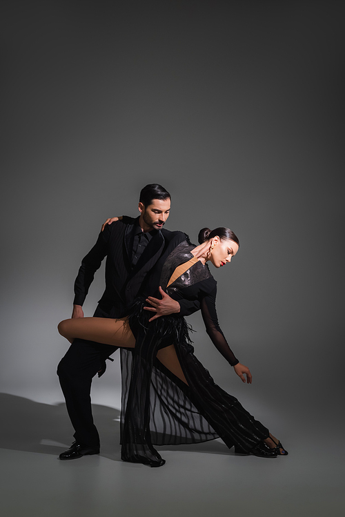 Elegant dancer hugging brunette partner in black dress on grey background with lighting