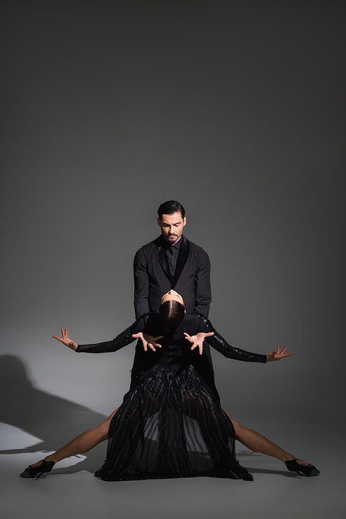 Dancer in suit performing tango with woman in black dress on grey background with shadow