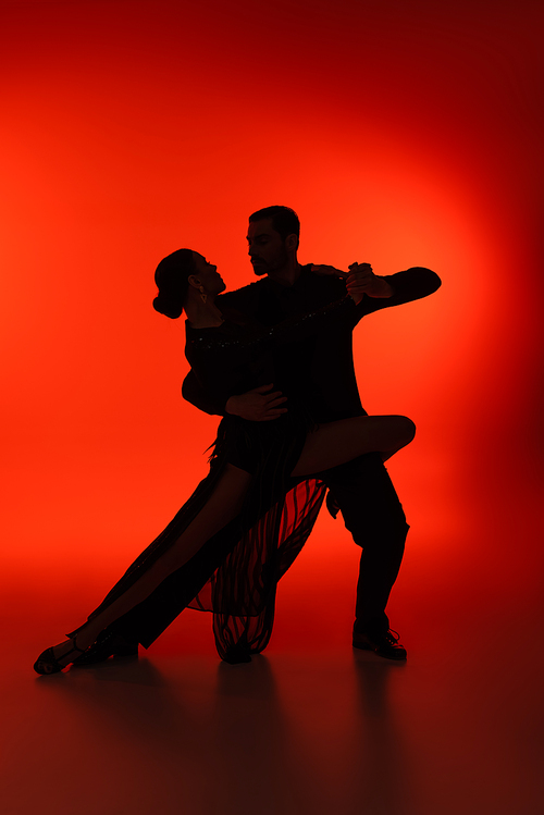 Silhouette of couple dancing tango on red background