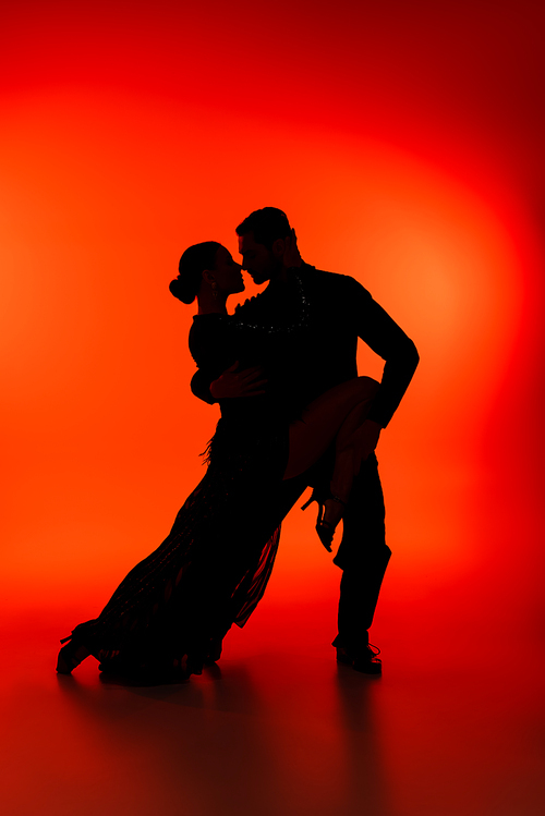 Side view of silhouette of couple dancing tango on red background