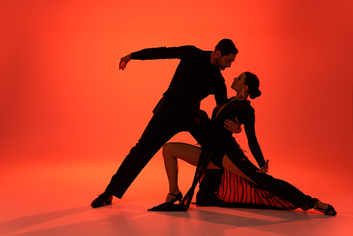 Side view of professional dancer hugging woman in dress on red background