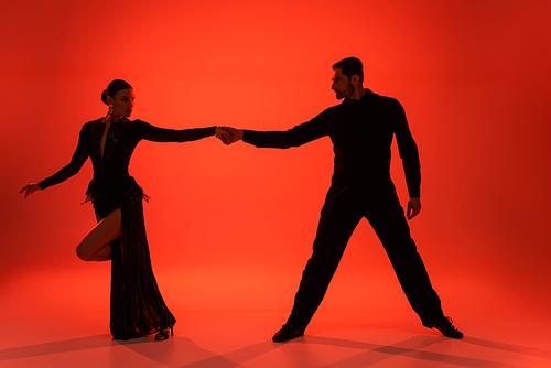 Silhouette of ballroom dancers holding hands on red background with shadow