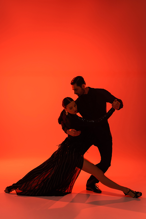 Silhouette of man in suit dancing tango with woman in dress on red background