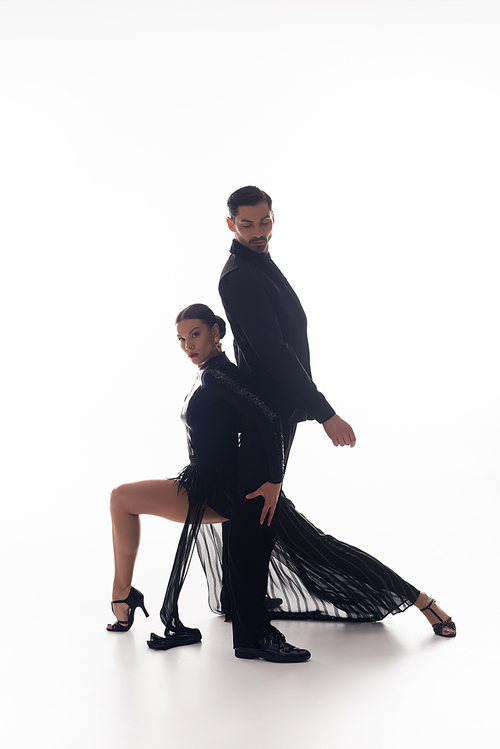 Elegant woman in black dress performing tango with partner on white background