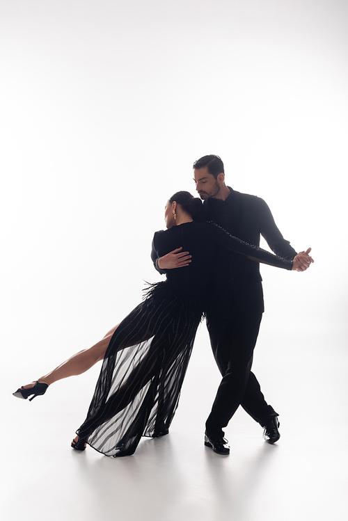 Man in suit performing tango with elegant woman on white background