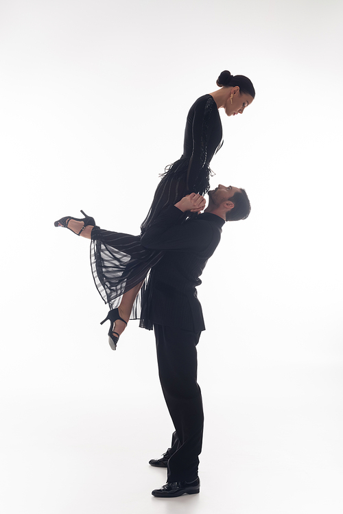 Side view of professional ballroom dancer lifting partner on white background