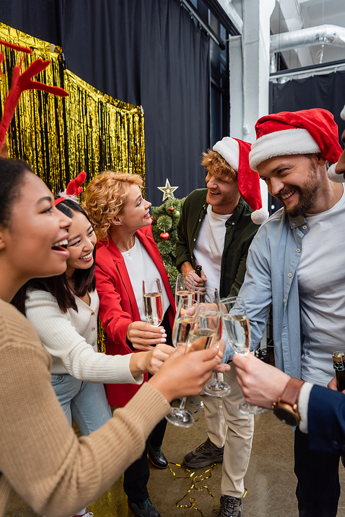 Multiethnic business people in santa hats holding champagne while celebrating Christmas in office