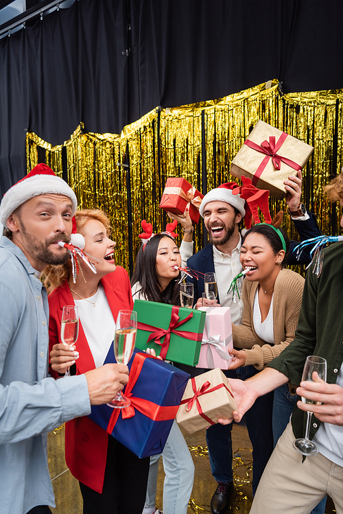 Cheerful interracial business people with party horns holding gifts and champagne in office