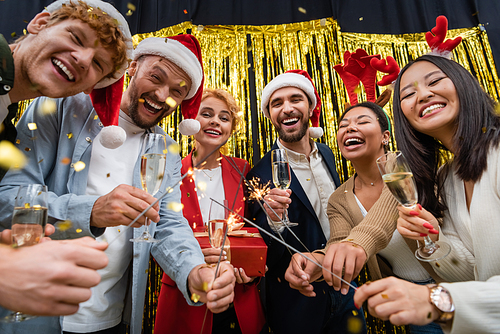 Low angle view of multiethnic business people holding sparklers and champagne during New Year party in office