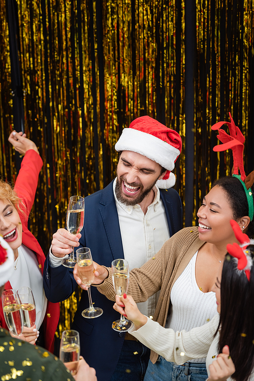 Interracial business people with champagne dancing under confetti during New Year party in office