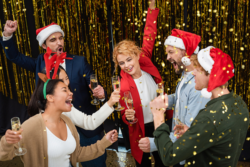 High angle view of multiethnic business people with champagne dancing near confetti and tinsel during corporate party in office