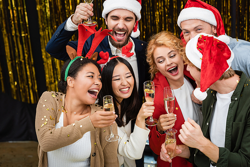 Multiethnic business people holding champagne under confetti during Christmas party in office