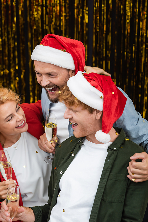Businessman in santa hat hugging colleagues with champagne during Christmas party in office
