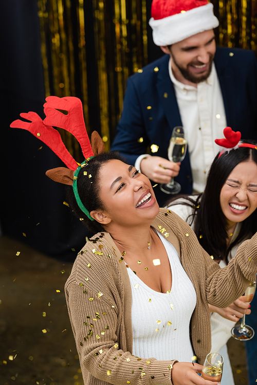 High angle view of multiracial businesswoman holding champagne under confetti during Christmas party in office