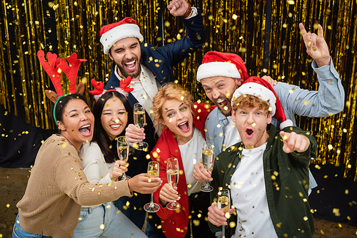 Positive multiethnic business people holding champagne under falling confetti in office