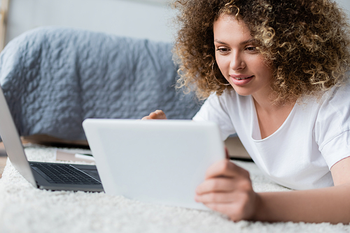 smiling woman using digital tablet on floor near laptop