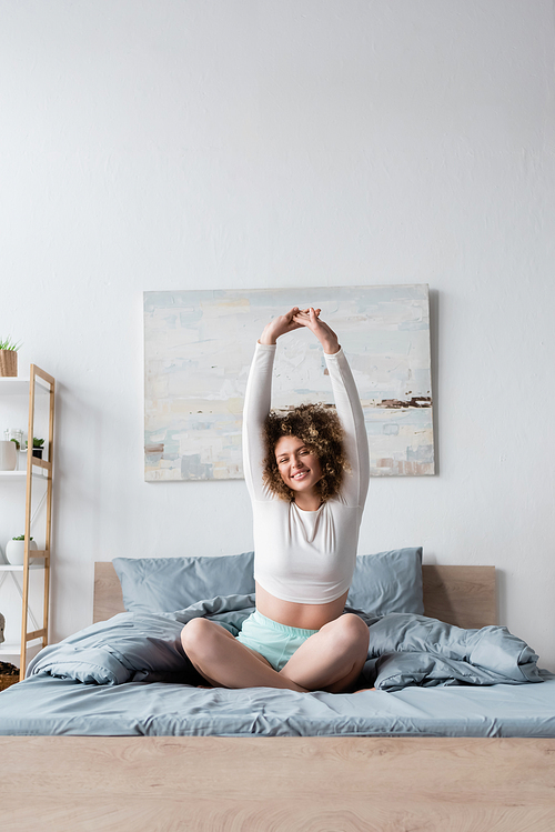 happy woman sitting on bed with crossed legs and stretching arms
