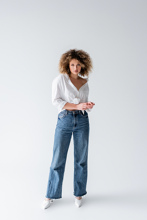 Full length of woman in jeans and blouse looking at camera on white background