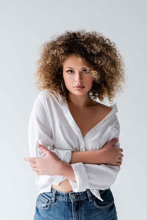 Portrait of young curly woman in blouse looking at camera isolated on white