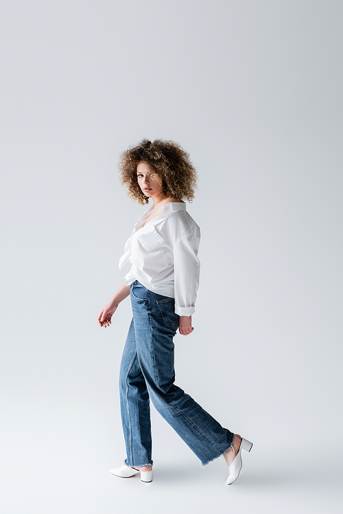 Trendy woman in jeans walking on white background