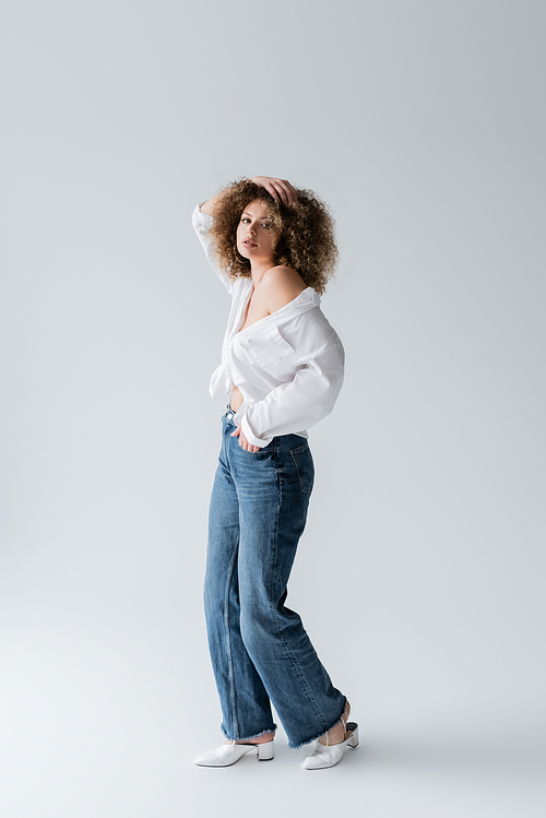 Full length of stylish woman holding hand in pocket of jeans on white background
