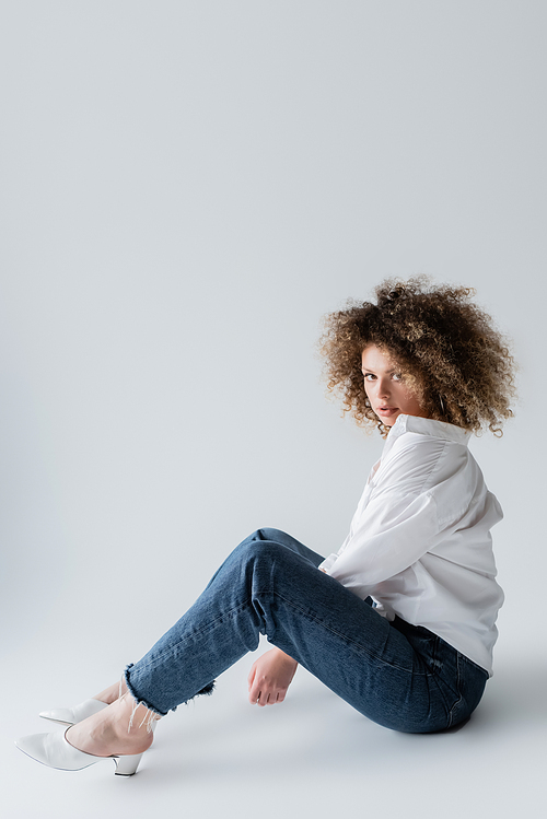 Trendy model in blouse and jeans sitting on white background